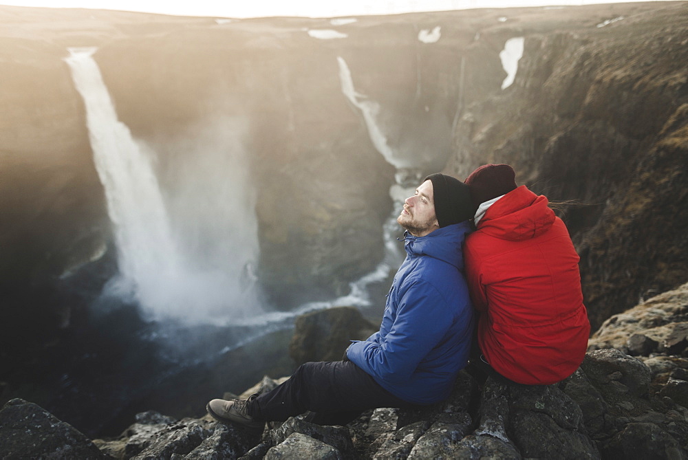 Hiker couple sitting on cliff by Haifoss waterfall in Iceland