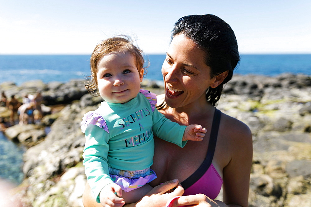 Woman holding baby daughter on rocks at beach