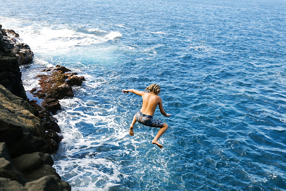 Boy jumping off cliff by sea