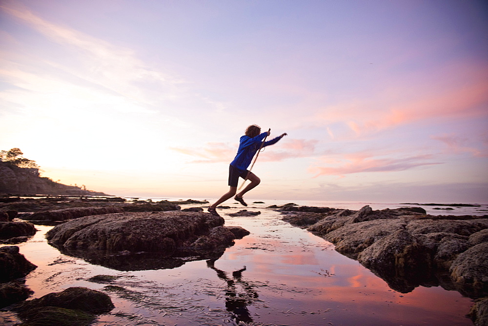 Teenage boy jumping between rocks of tide pool in La Jolla, California