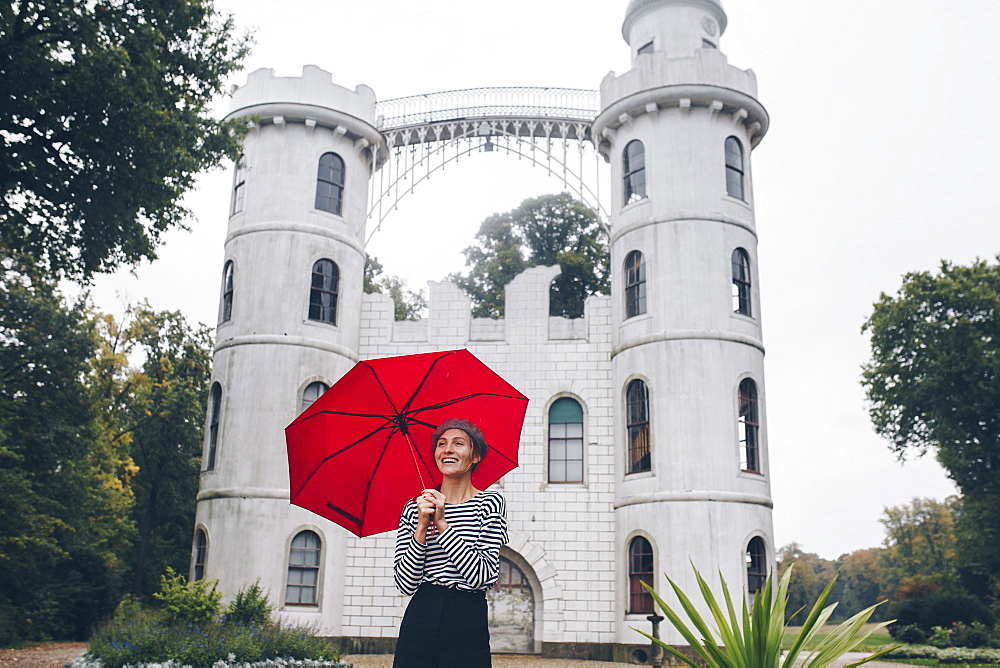 Woman holding red umbrella by Schloss Pfaueninsel in Potsdam, Germany