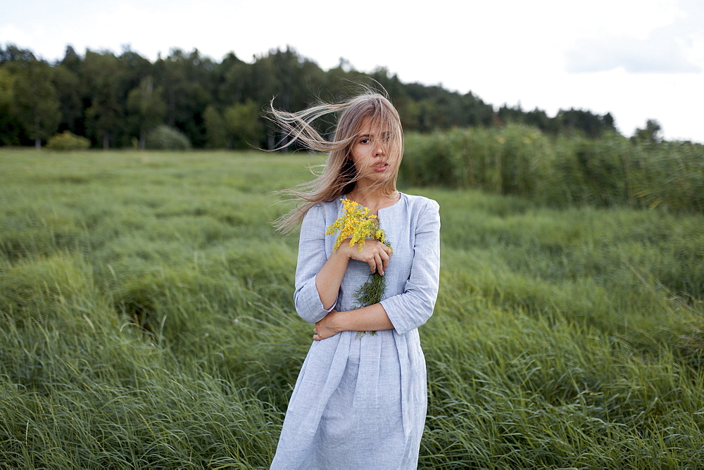 Windswept woman holding yellow flowers in field