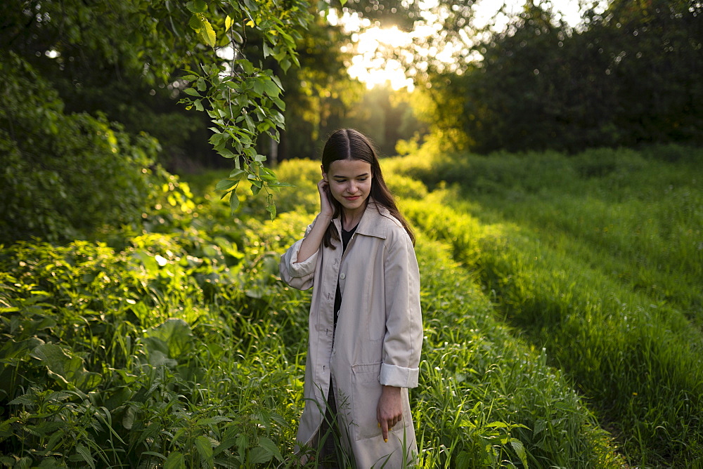 Teenage girl wearing gray coat in field at sunset