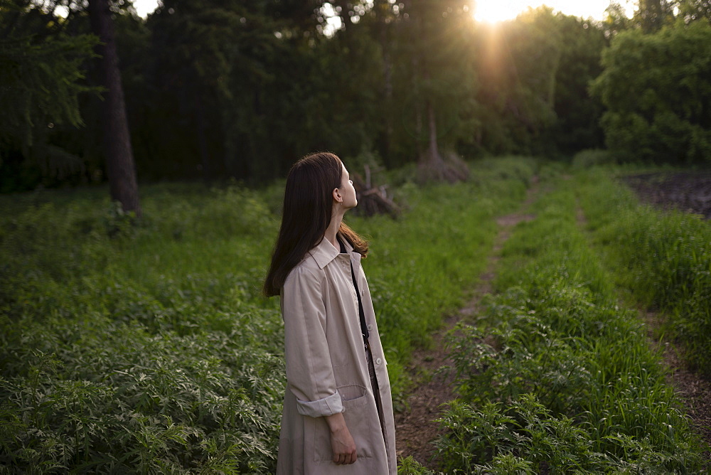 Teenage girl wearing gray coat in field at sunset