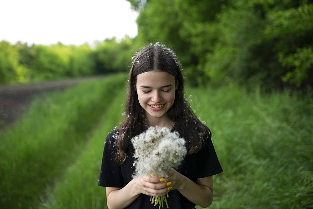 Smiling teenage girl holding dandelions in a field