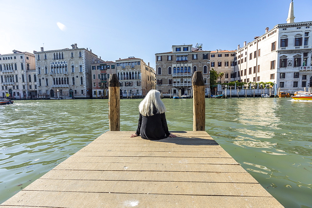 Woman sitting on jetty on Grand Canal in Venice, Italy