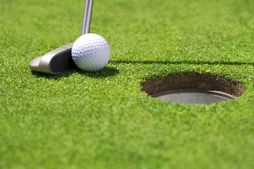 Closeup of golf ball and club near cup