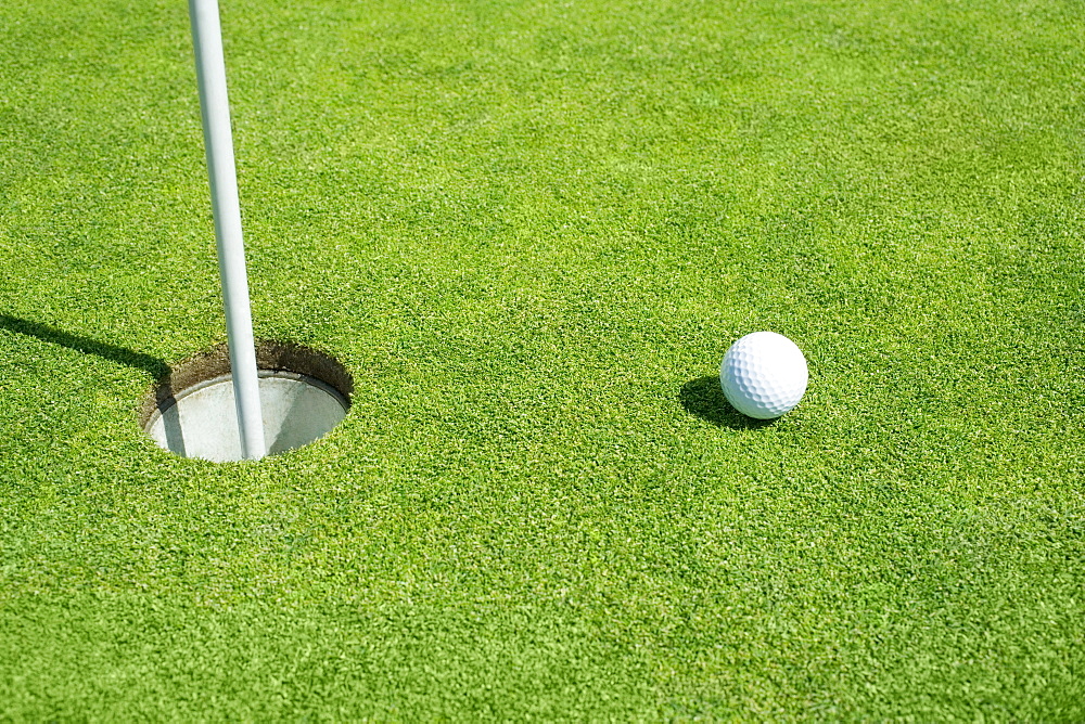 Golf ball near cup on putting green outdoors