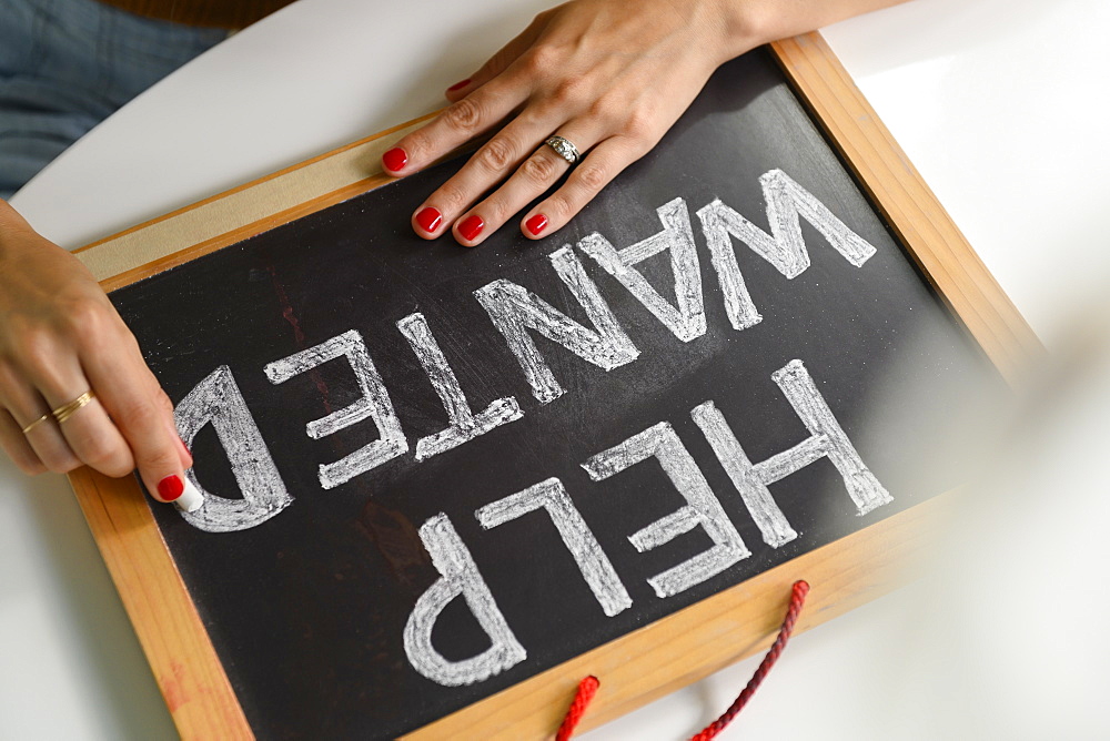 Woman writing 'Help Wanted' on chalkboard