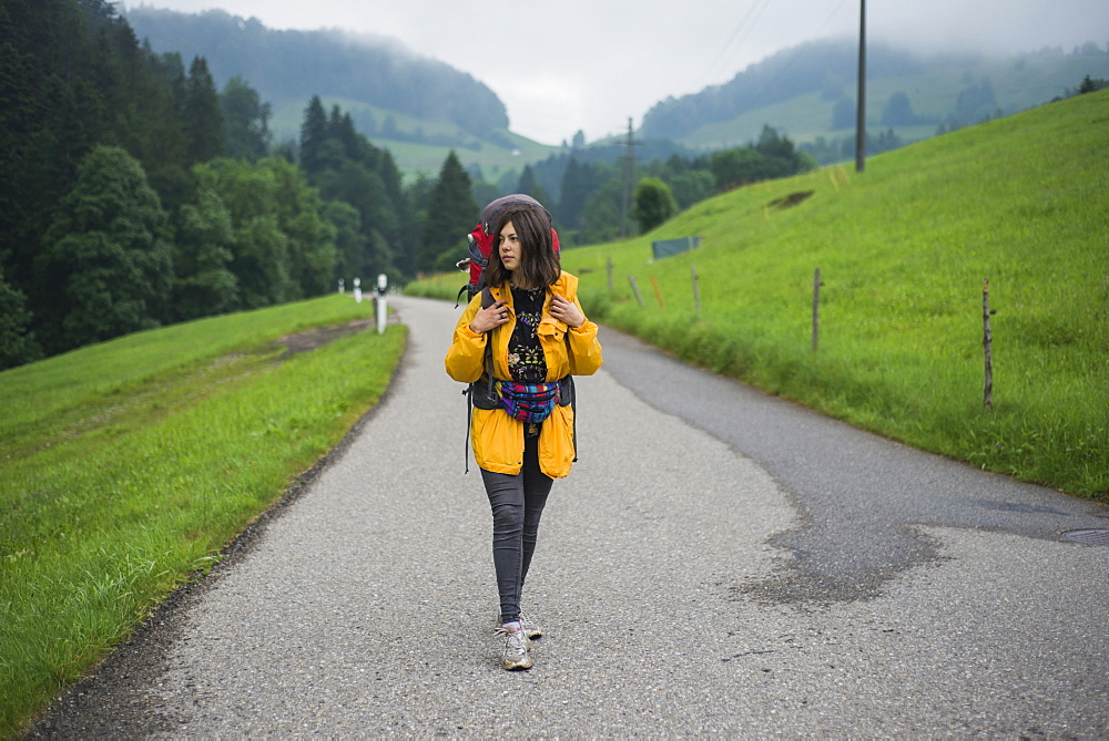 Young woman with yellow jacket and backpack walking along country road