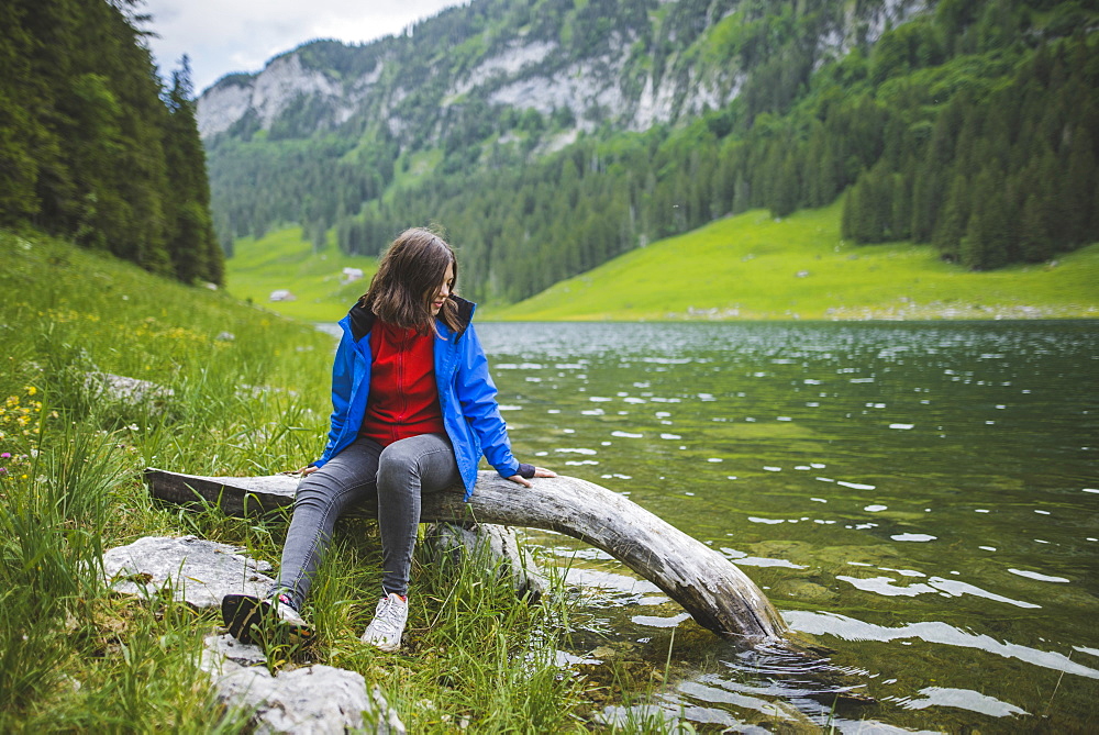 Young woman sitting on log by lake