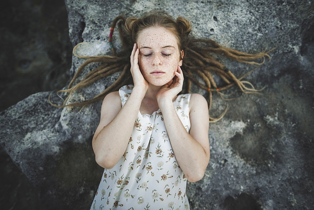 Young woman with dreadlocks lying on rock