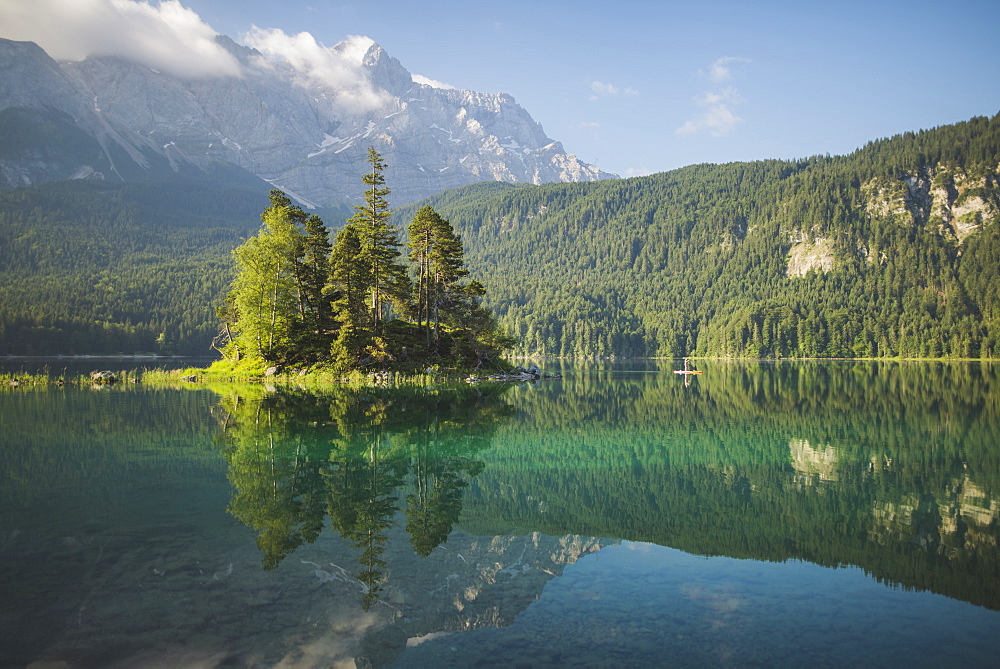 Germany, Bavaria, Eibsee, Distant view of woman paddleboarding on the lake Eibsee in Bavarian Alps at sunrise