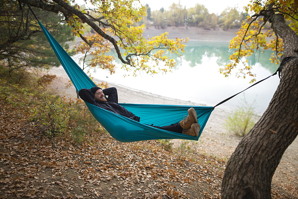 Italy, Smiling man lying in hammock near lake