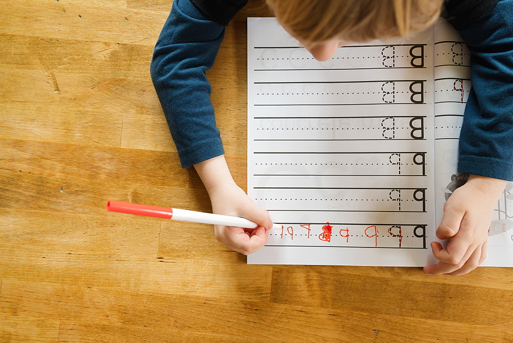 Overhead view of boy (4-5) practicing writing letters in workbook