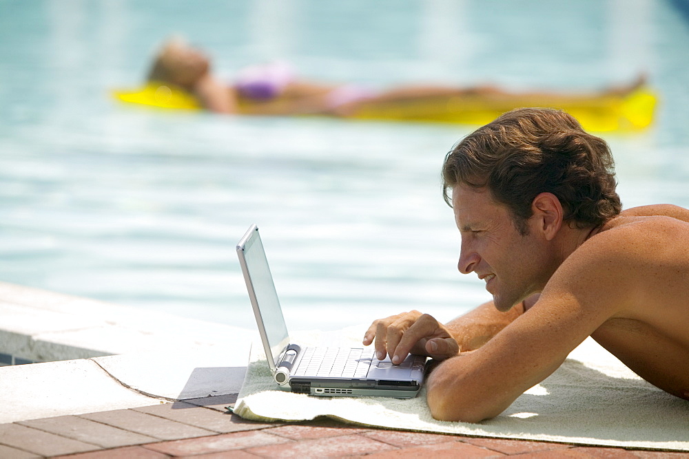 A man poolside using a laptop computer