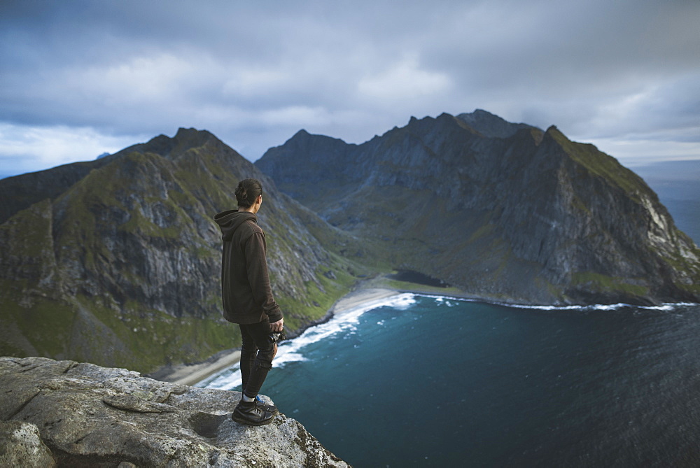 Man holding camera on cliff at Ryten mountain in Lofoten Islands, Norway