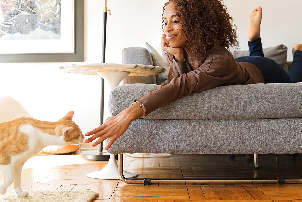 Smiling woman on sofa reaching out to cat