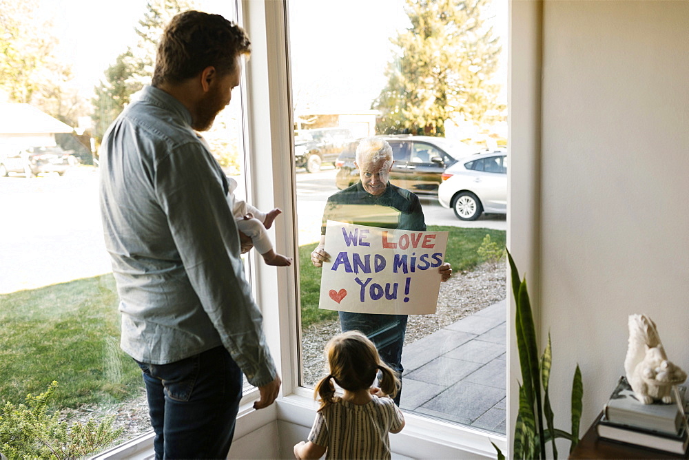 Grandfather showing message to family with grandchildren (2-3 months, 2-3) through window