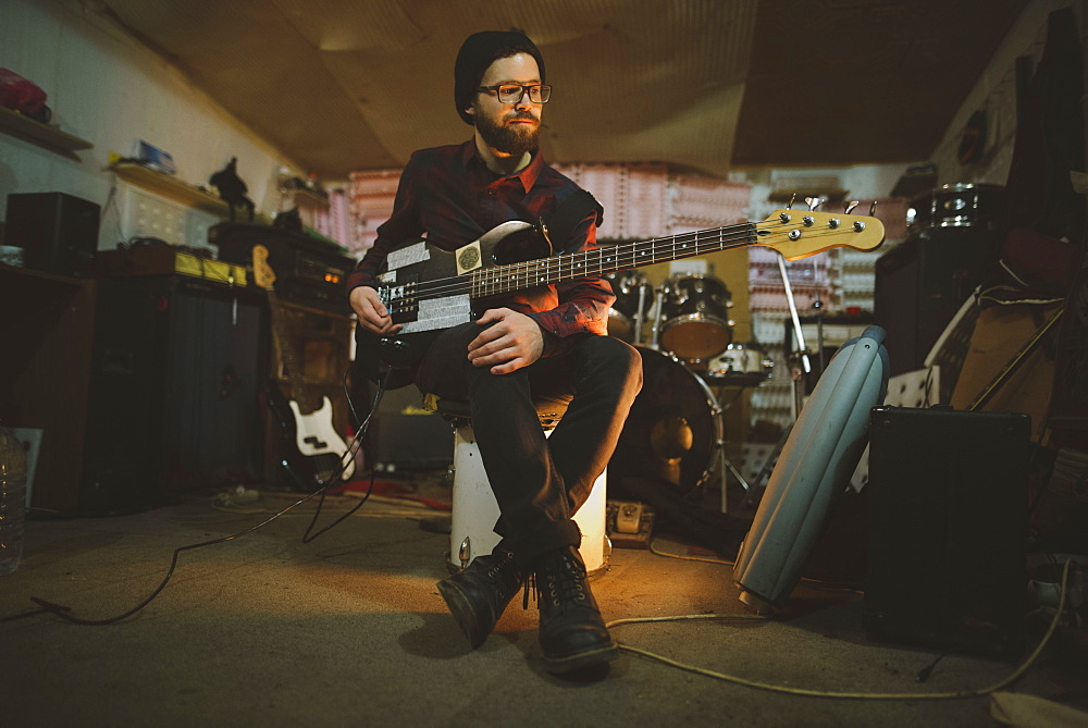 Young man playing bass guitar during rehearsal in garage