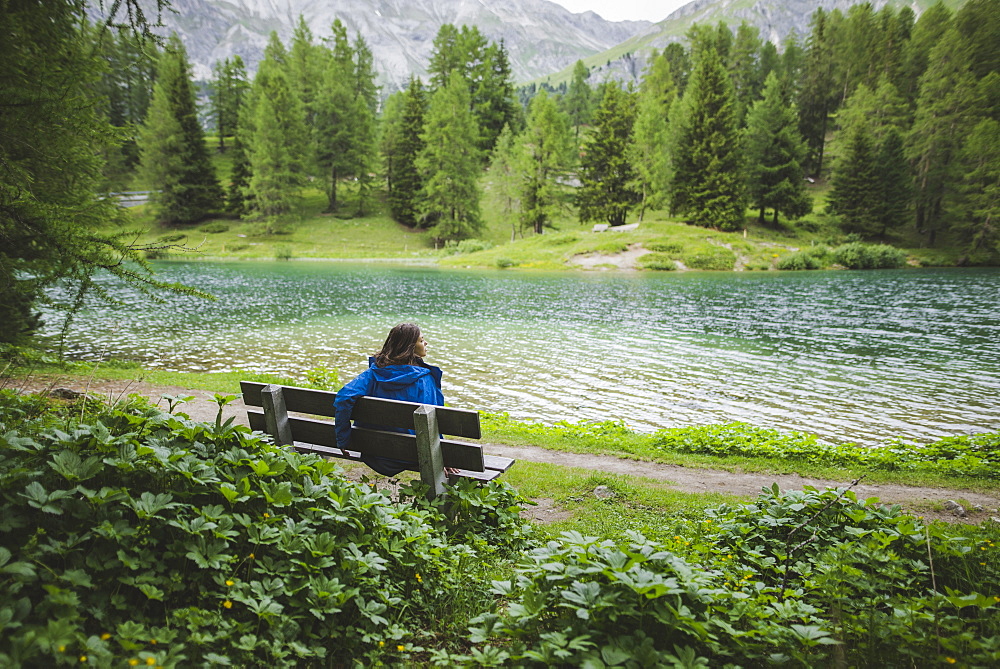 Switzerland, Bravuogn, Palpuognasee, Young woman resting on bench near Palpuognasee lake in Swiss Alps