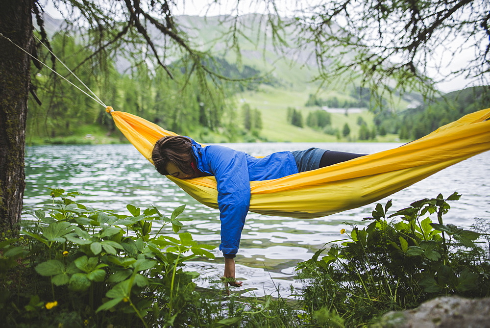 Switzerland, Bravuogn, Palpuognasee, Young woman resting in hammock near Palpuognasee lake in Swiss Alps