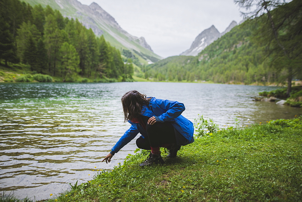 Switzerland, Bravuogn, Palpuognasee, Young woman crouching by Palpuognasee lake in Swiss Alps