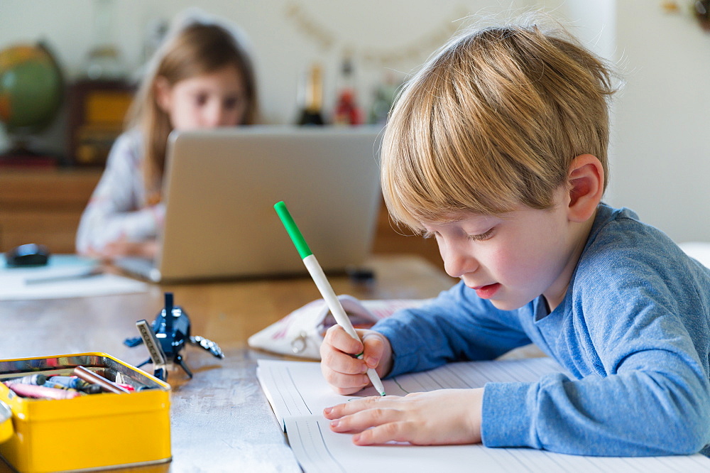 Boy (4-5) and girl (6-7) doing homework at table