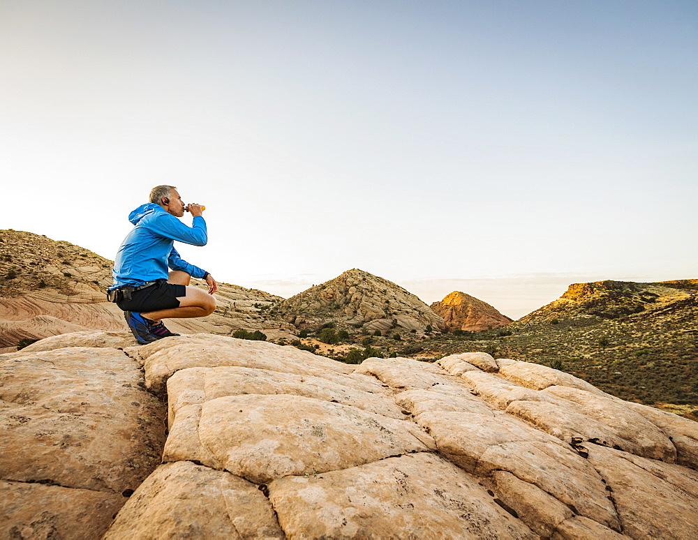 USA, Utah, St. George, Man crouching in rocky landscape and drinking water after running