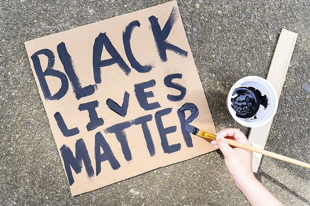 Woman's hand painting Black Lives Matter sign on cardboard