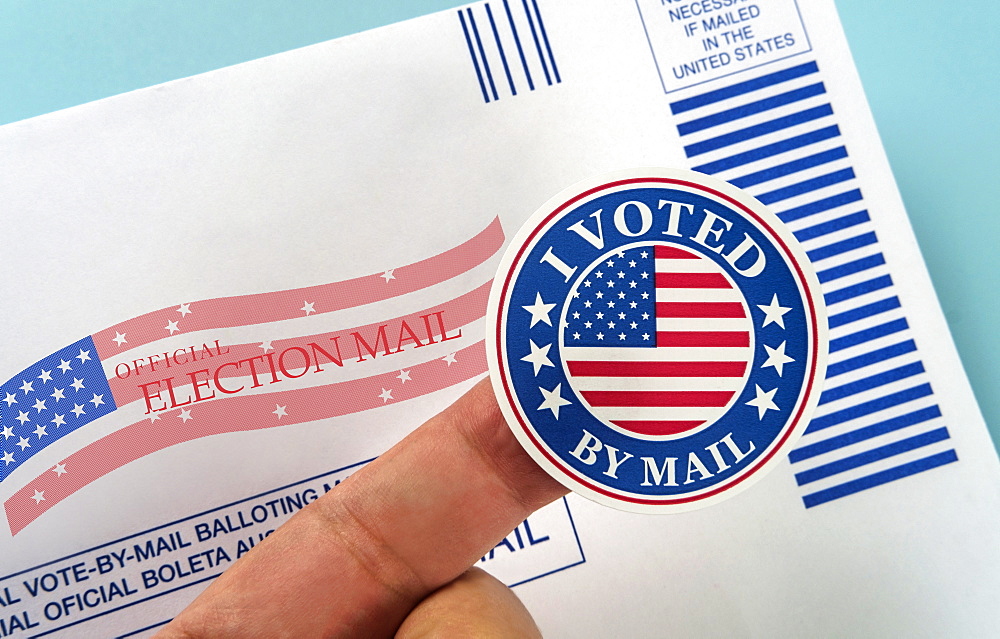 Human finger holding sticker above voting mail