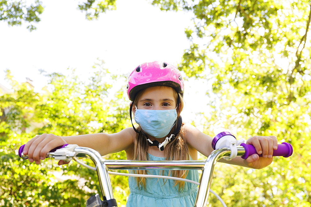 Girl (6-7) wearing flu mask and riding bicycle