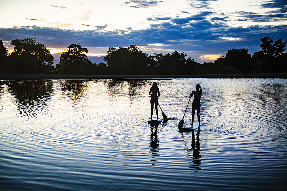 USA, Utah, Salem, Two teenage girls (14-15) on stand up paddle bards on lake at dusk