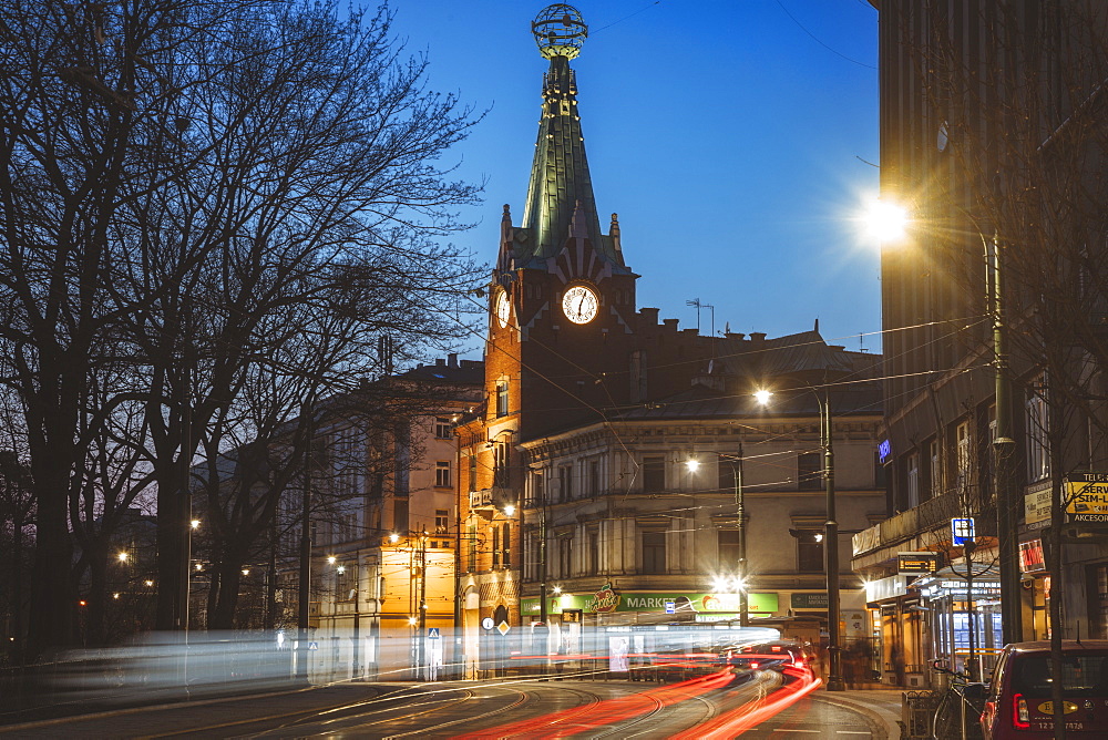 Poland, Lesser Poland, Krakow, Illuminated city street with clock tower at night