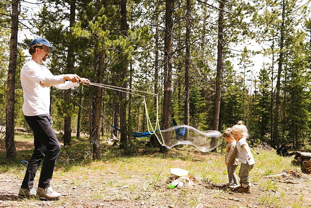 Father making large soap bubbles in forest for two daughters (2-3, 4-5), Wasatch-Cache National Forest