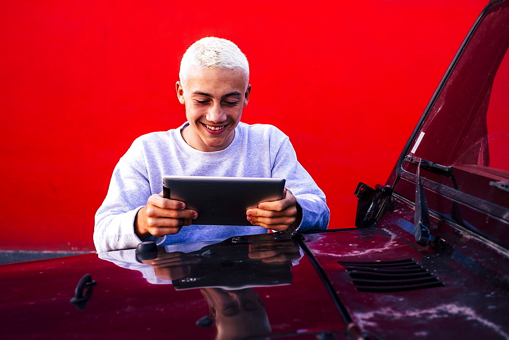 Teenager (16-17) using tablet leaning against car