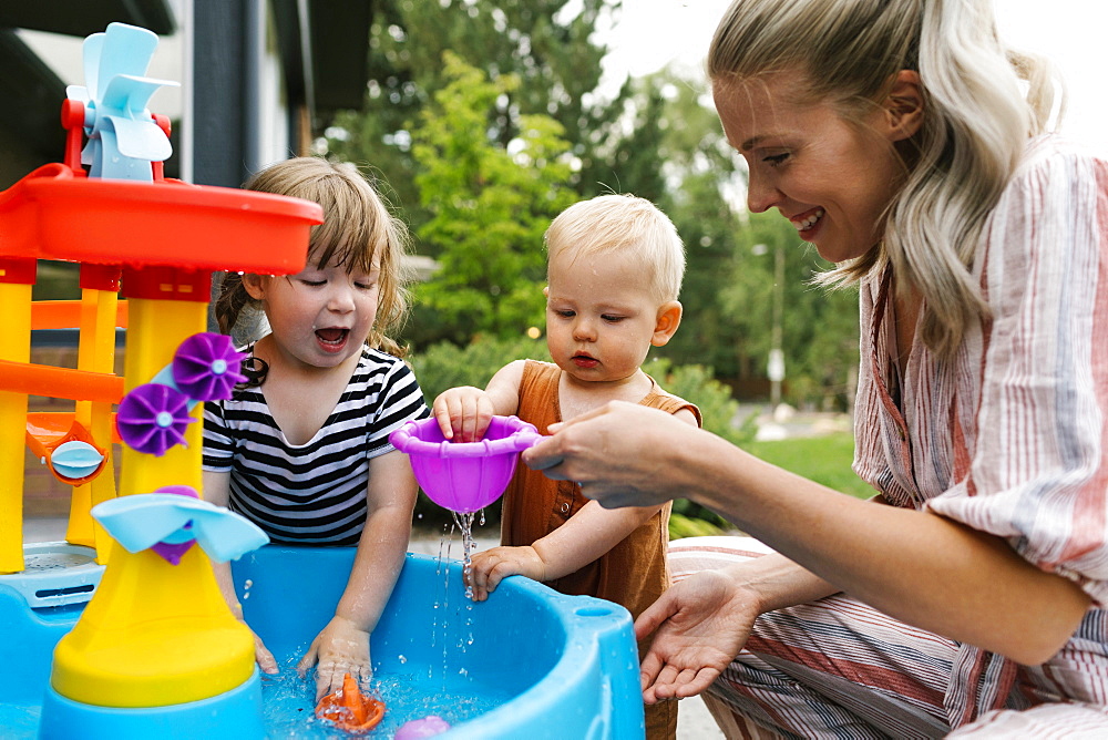 Mother with baby son (18-23 months) and toddler daughter(2-3)playing with water in garden