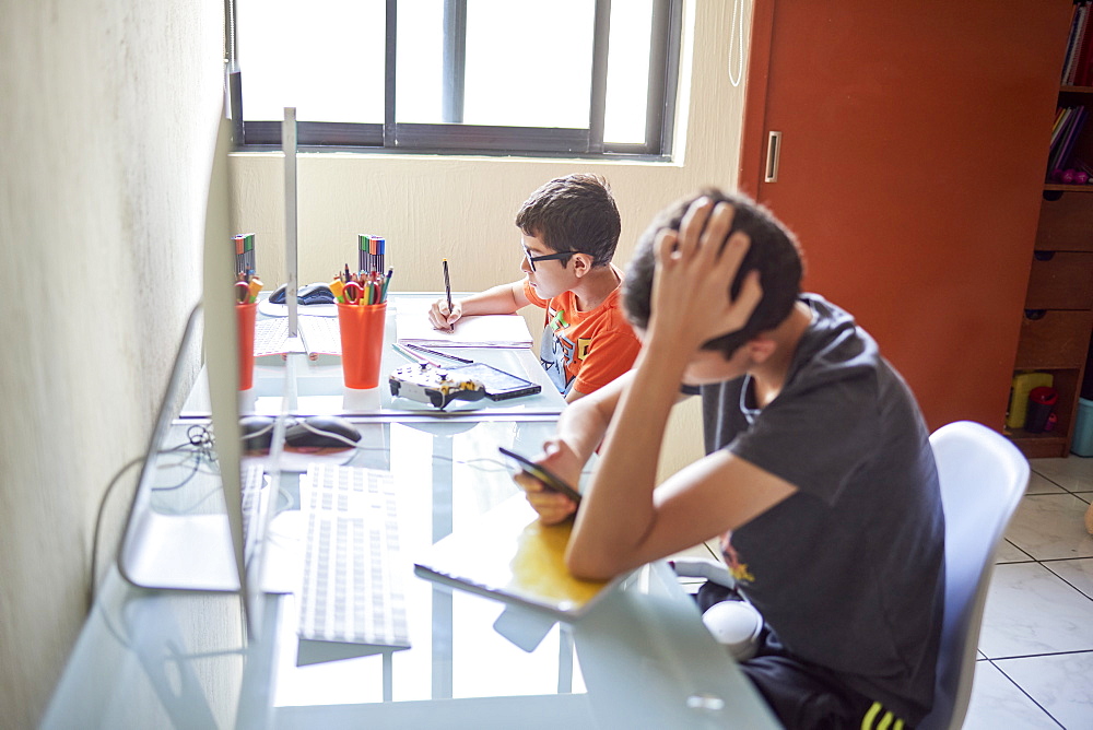 Two boys (8-9, 14-15) learning at desk at home during Covid-19 lockdown