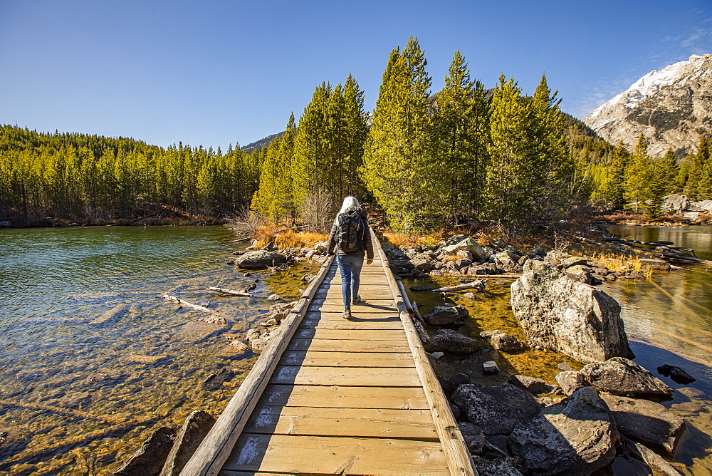 USA, Wyoming, Jackson, Grand Teton National Park, Senior woman walking on wooden path over Taggart Lake in Grand Teton National Park