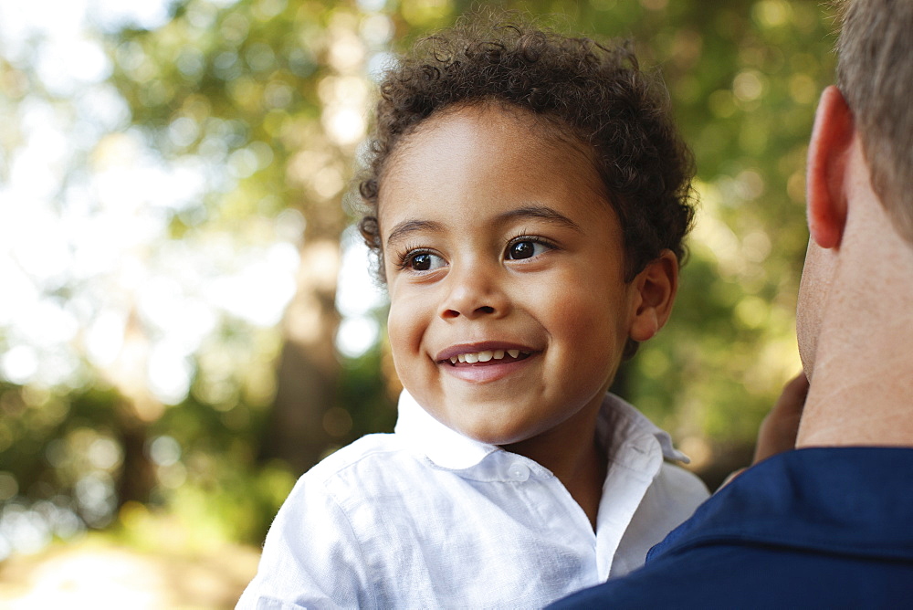 Over shoulder view of father carrying preschool boy looking away smiling