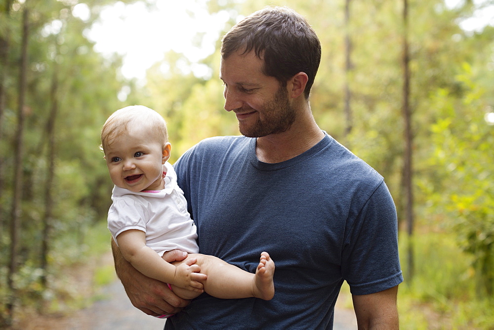 Happy mid adult man carrying baby daughter on forest track
