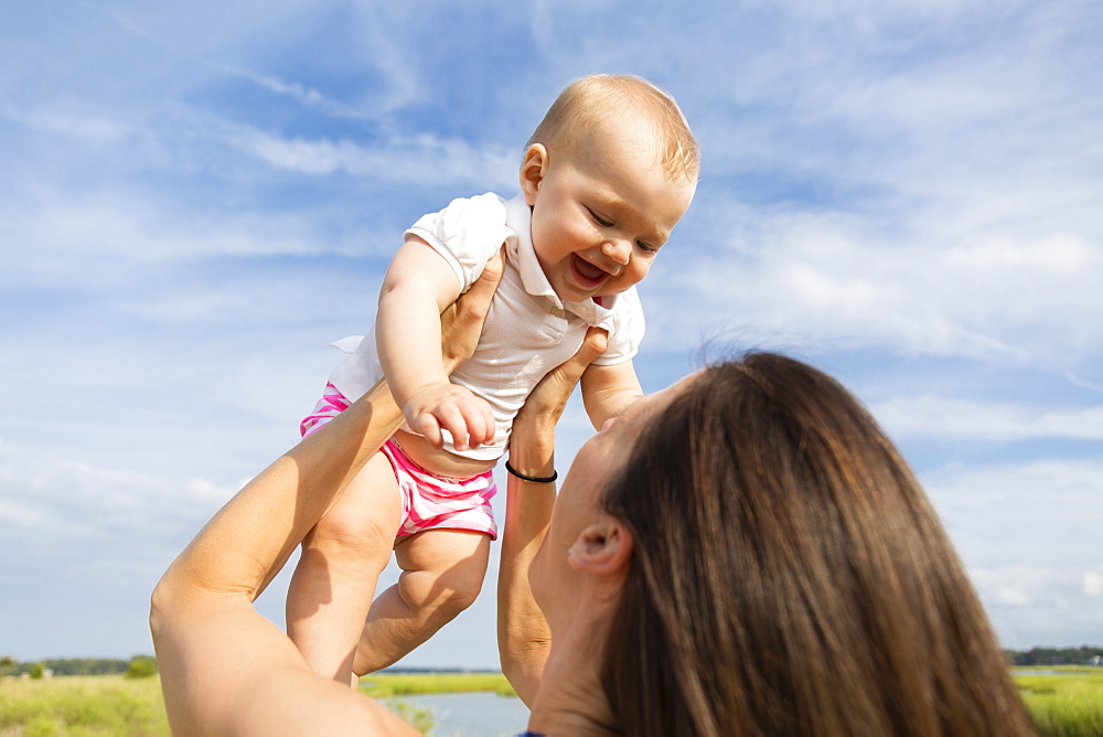 Mid adult woman holding up baby daughter on riverside