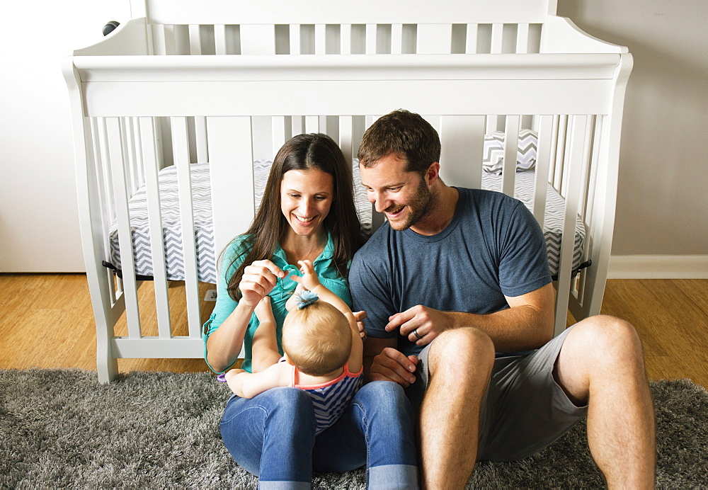 Mid adult couple playing with baby daughters fingers on lap