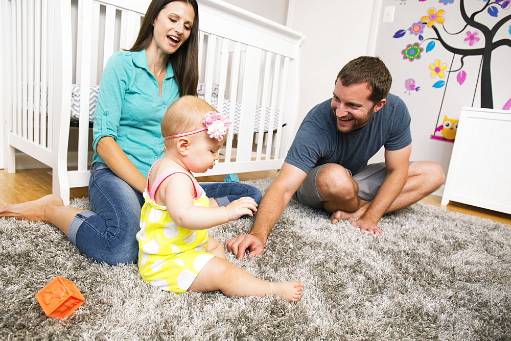 Mid adult couple playing with baby daughter on nursery rug