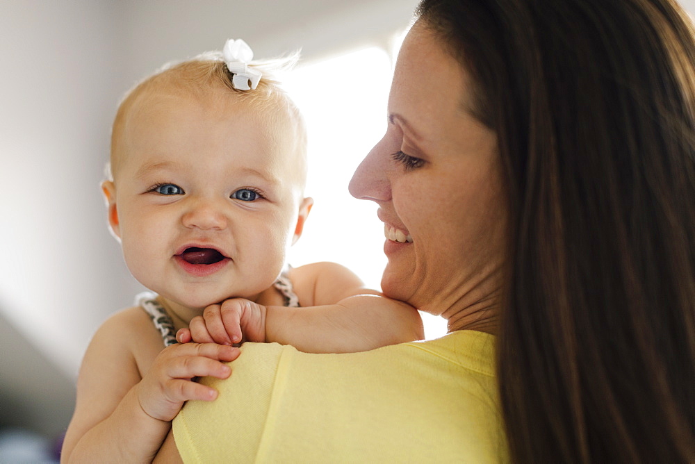 Over the shoulder portrait view of happy baby girl and mid adult mother