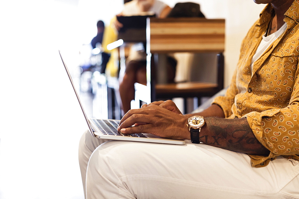Young man in coffee shop, using laptop, mid section