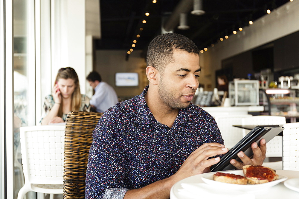 Young man in coffee shop, using digital tablet