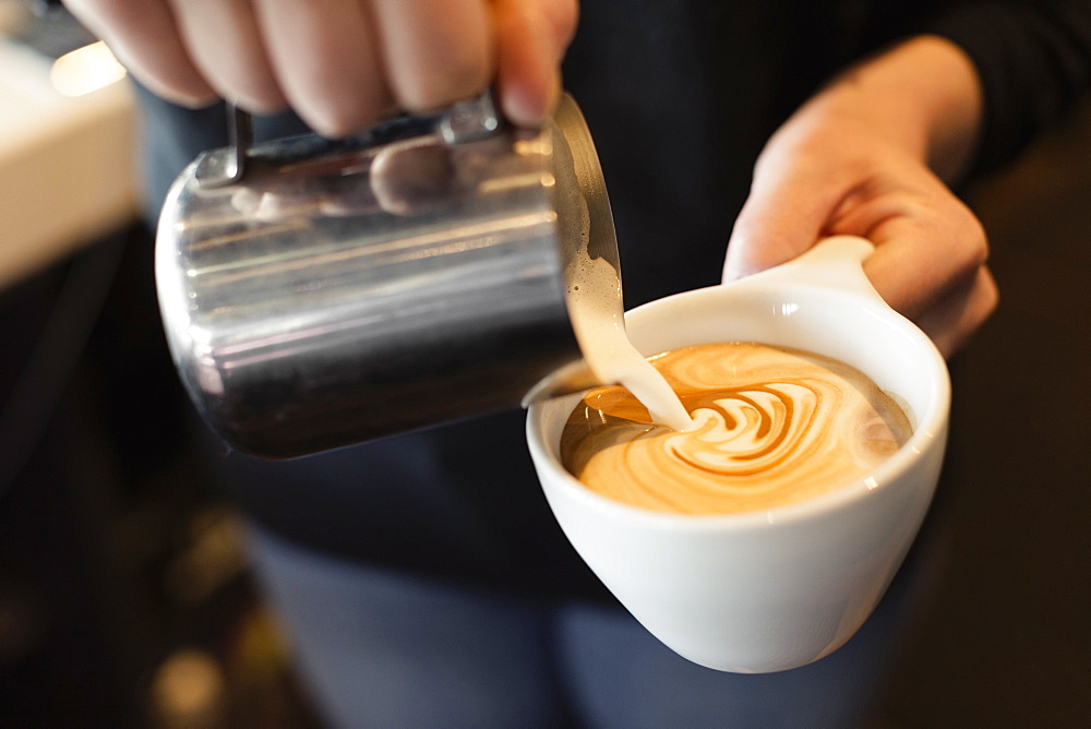 Coffee shop barista pouring milk into coffee, mid section, close-up