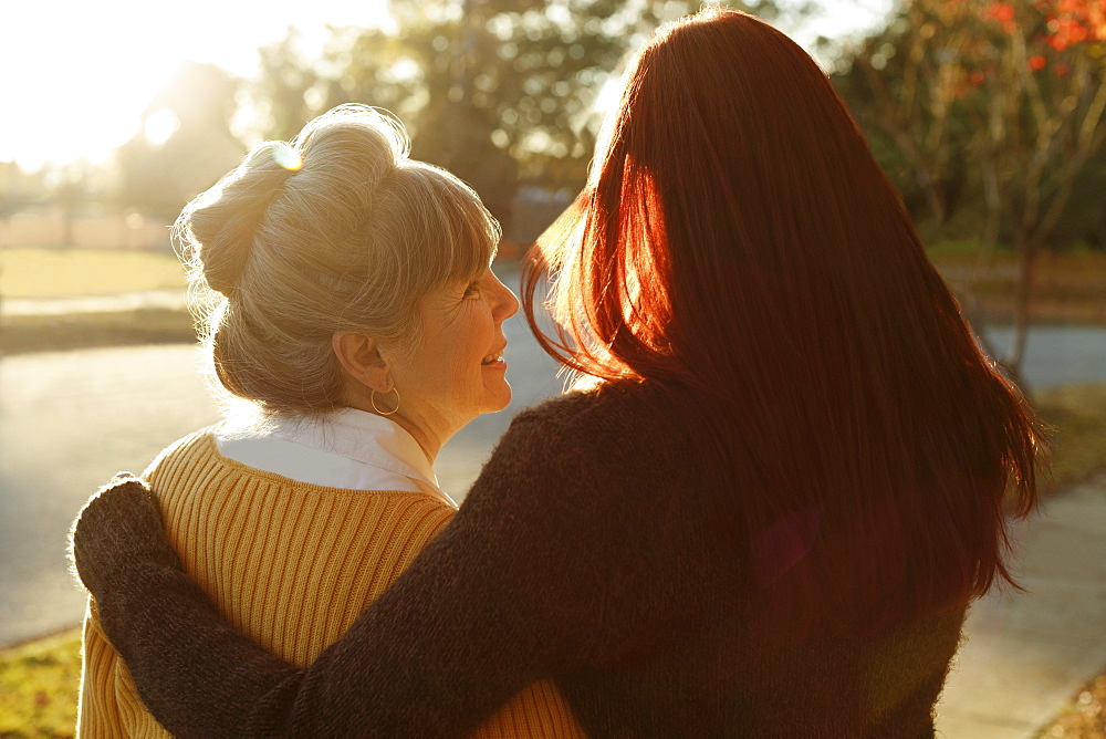 Rear view of senior woman and adult daughter strolling in park