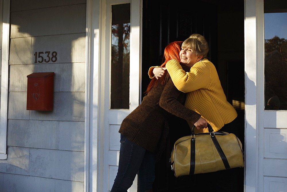 Senior woman and adult daughter hugging at front door